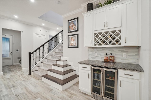 bar featuring white cabinets, dark stone countertops, ornamental molding, and wine cooler