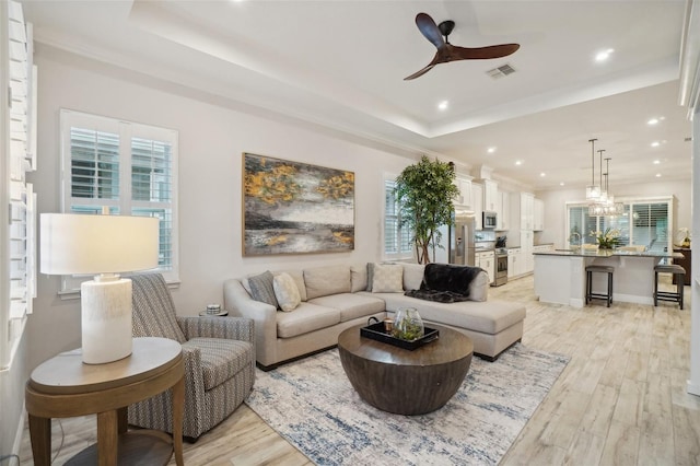 living room featuring a raised ceiling, ceiling fan, and light hardwood / wood-style floors