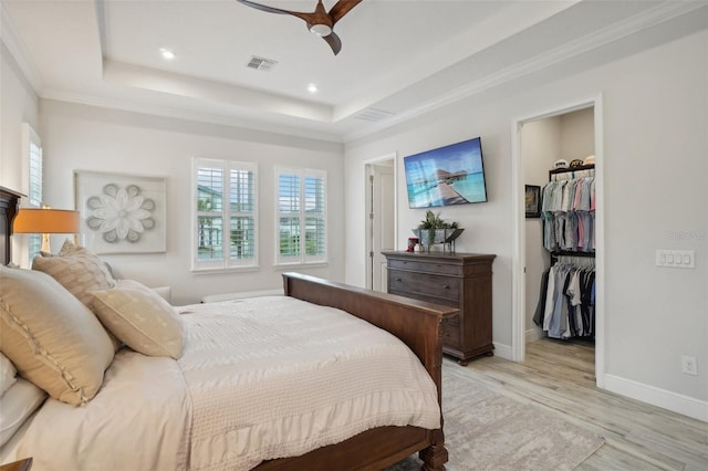 bedroom featuring a spacious closet, ceiling fan, light hardwood / wood-style floors, a tray ceiling, and a closet