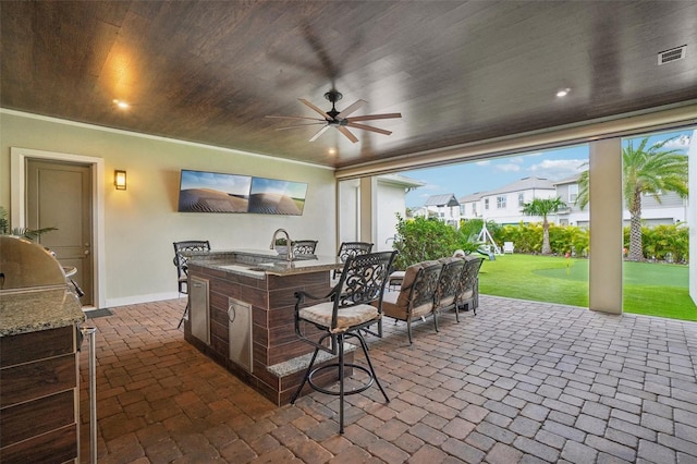 view of patio / terrace featuring a wet bar, ceiling fan, and an outdoor kitchen