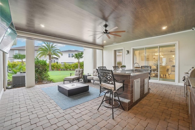 view of patio / terrace with an outdoor hangout area, ceiling fan, central AC unit, a wet bar, and exterior kitchen