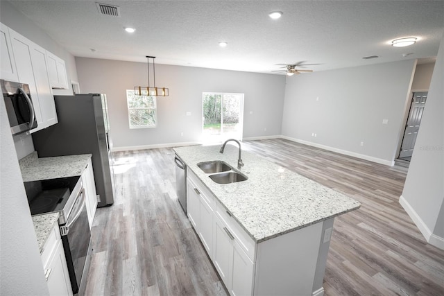 kitchen with appliances with stainless steel finishes, sink, white cabinets, hanging light fixtures, and an island with sink