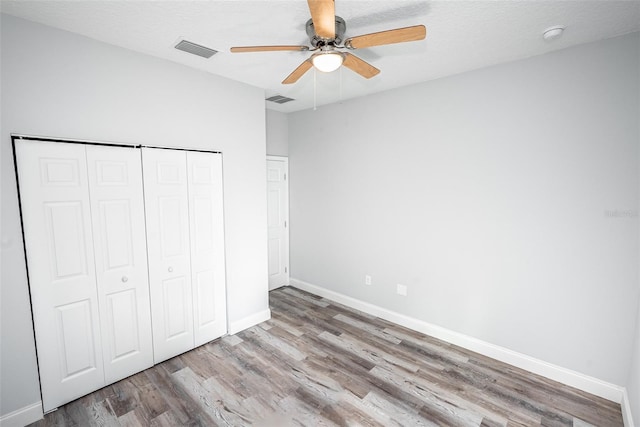 unfurnished bedroom featuring ceiling fan, a closet, wood-type flooring, and a textured ceiling