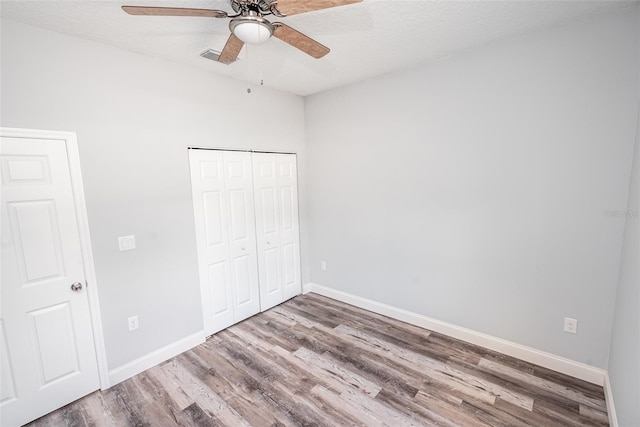 unfurnished bedroom with wood-type flooring, a textured ceiling, a closet, and ceiling fan