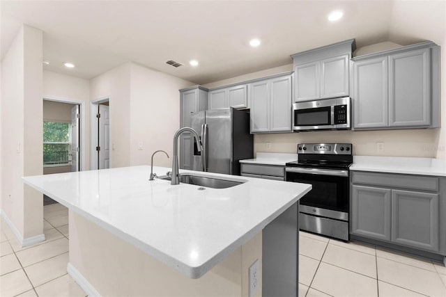 kitchen featuring stainless steel appliances, gray cabinets, a kitchen island with sink, and sink