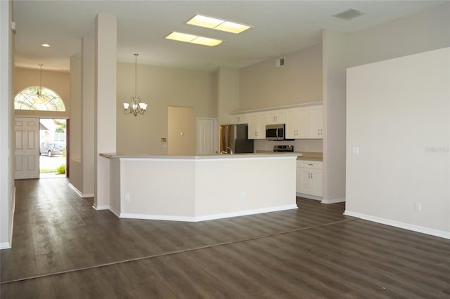 kitchen with white cabinets, a notable chandelier, dark wood-style flooring, appliances with stainless steel finishes, and a towering ceiling