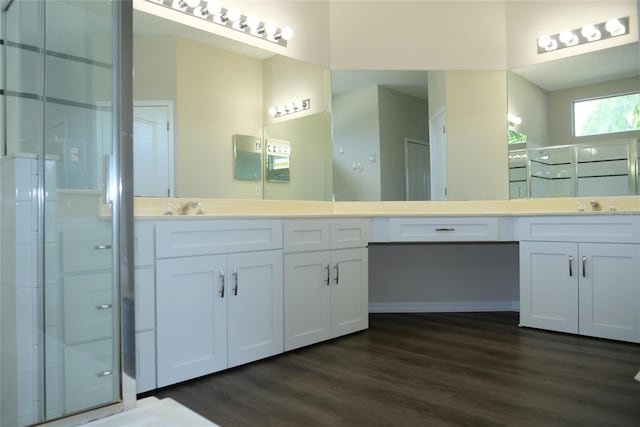 bathroom with a shower stall, wood finished floors, double vanity, and a sink