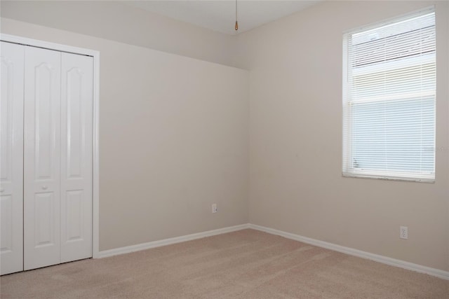 unfurnished bedroom with a closet, baseboards, and light carpet