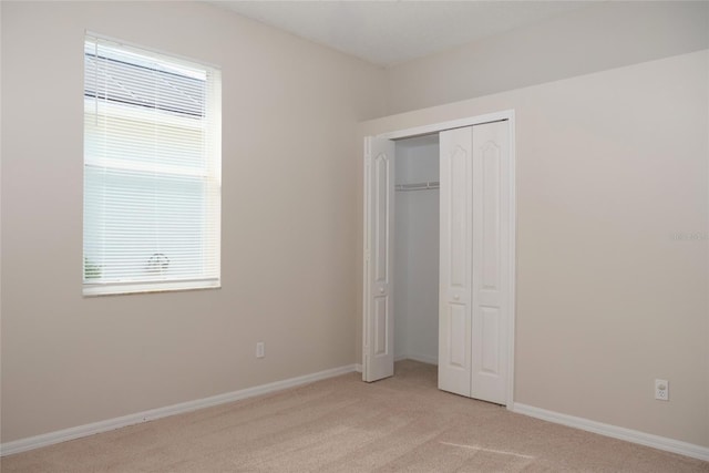 unfurnished bedroom featuring a closet, baseboards, multiple windows, and light colored carpet