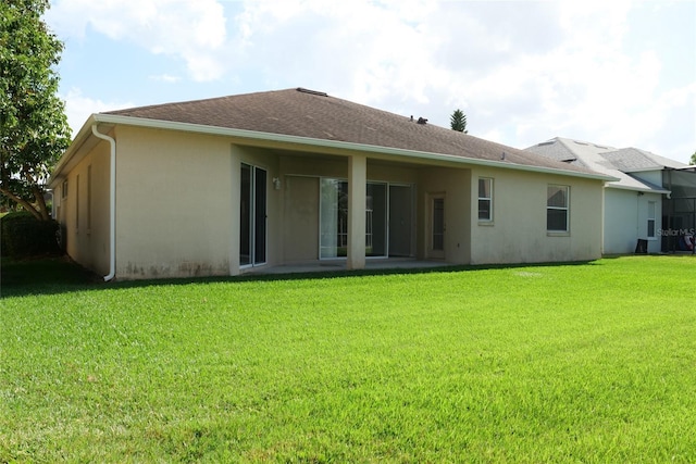 back of house featuring a shingled roof, stucco siding, and a lawn