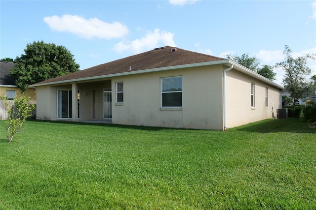 rear view of house featuring a yard, central air condition unit, and stucco siding