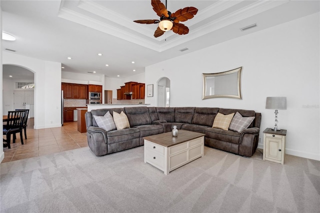 living room with a raised ceiling, light carpet, crown molding, and ceiling fan