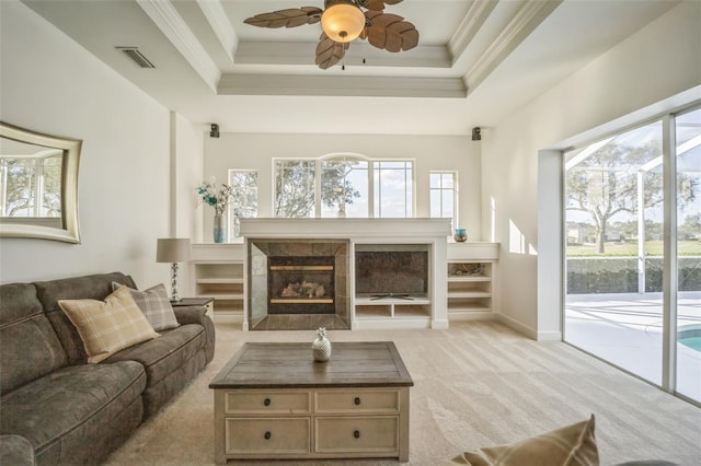 living room featuring light carpet, ornamental molding, a raised ceiling, ceiling fan, and a tiled fireplace