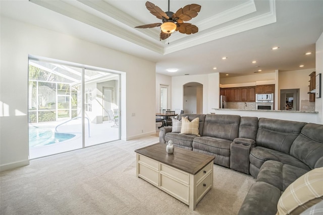 carpeted living room with a raised ceiling, ceiling fan, and ornamental molding