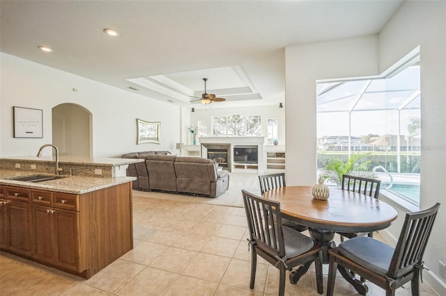 tiled dining room with a raised ceiling, ceiling fan, and sink