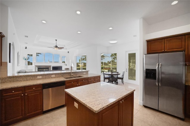 kitchen with light stone countertops, sink, a raised ceiling, a kitchen island, and appliances with stainless steel finishes