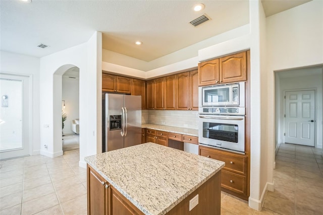 kitchen featuring light stone countertops, a center island, stainless steel appliances, backsplash, and light tile patterned flooring