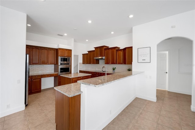 kitchen featuring light stone countertops, a center island, stainless steel appliances, backsplash, and kitchen peninsula