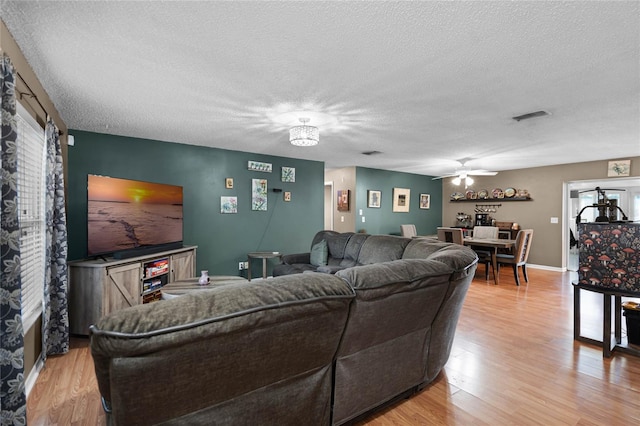 living room featuring ceiling fan, a textured ceiling, and light hardwood / wood-style flooring