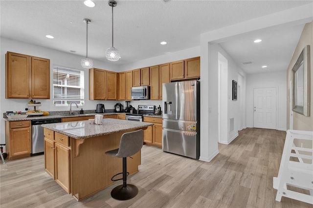 kitchen with appliances with stainless steel finishes, light wood-type flooring, a breakfast bar, pendant lighting, and a center island