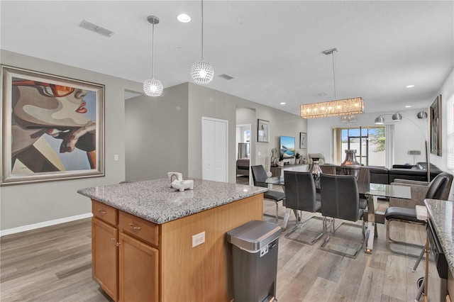 kitchen with decorative light fixtures, a kitchen island, and light hardwood / wood-style flooring