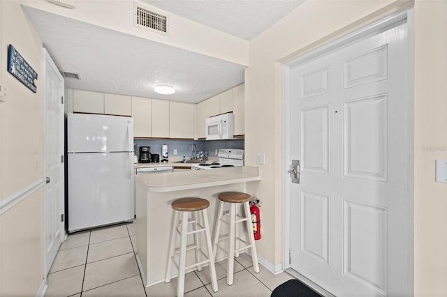 kitchen featuring kitchen peninsula, a breakfast bar, a textured ceiling, white appliances, and sink