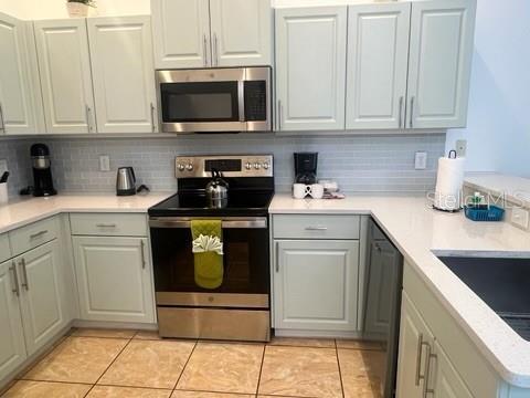 kitchen featuring appliances with stainless steel finishes, backsplash, sink, light tile patterned floors, and gray cabinets