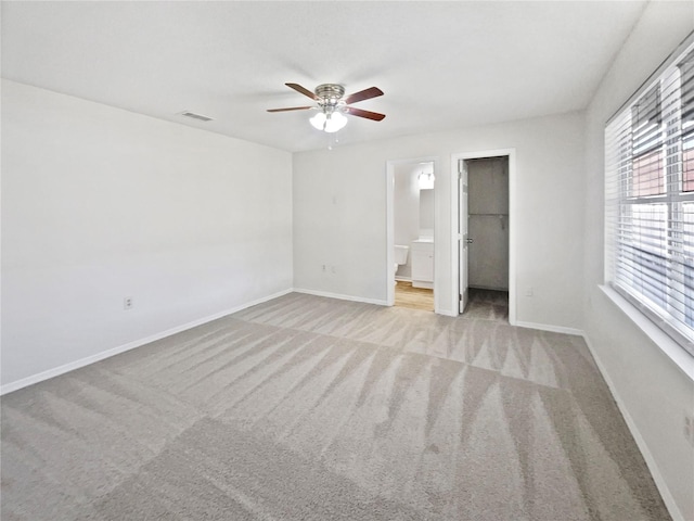 unfurnished bedroom with ensuite bathroom, light colored carpet, ceiling fan, a spacious closet, and a closet