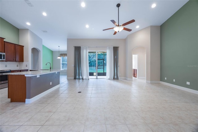 kitchen with light stone counters, stainless steel appliances, ceiling fan, light tile patterned floors, and an island with sink