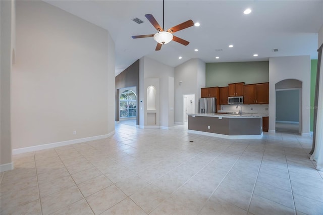 kitchen featuring ceiling fan, stainless steel appliances, high vaulted ceiling, a kitchen island with sink, and light tile patterned flooring