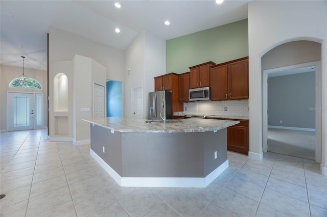 kitchen featuring a towering ceiling, an island with sink, light tile patterned flooring, and appliances with stainless steel finishes