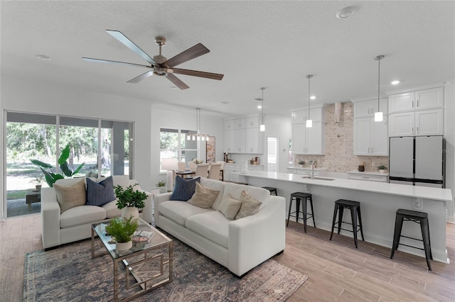 living room featuring a textured ceiling, ceiling fan, sink, and light hardwood / wood-style flooring