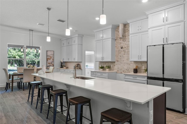 kitchen with stainless steel refrigerator, a large island with sink, white cabinetry, and hanging light fixtures