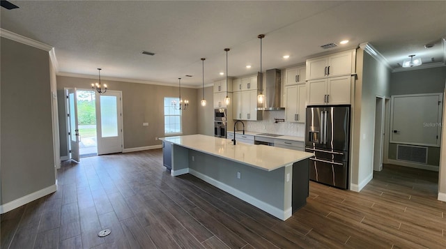 kitchen featuring decorative light fixtures, light countertops, appliances with stainless steel finishes, a large island with sink, and wall chimney exhaust hood