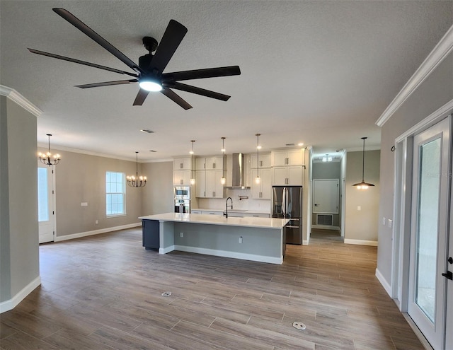 kitchen featuring wall chimney exhaust hood, stainless steel appliances, a sink, and pendant lighting