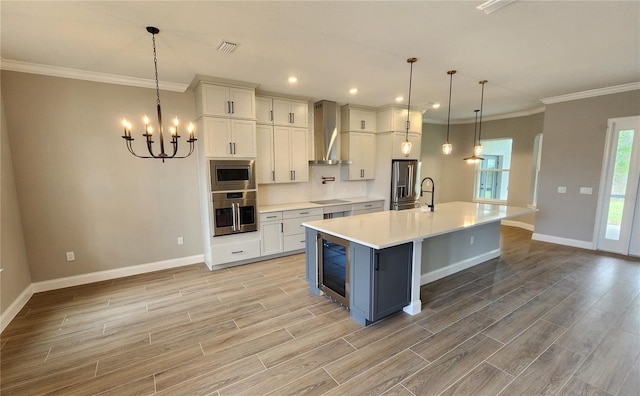 kitchen with a spacious island, light countertops, hanging light fixtures, appliances with stainless steel finishes, and wall chimney range hood