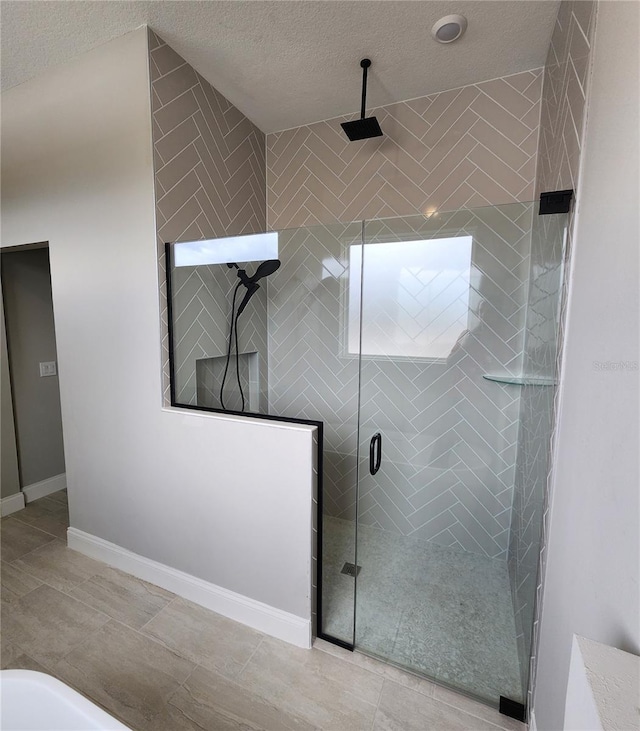 full bath with a textured ceiling, a stall shower, and baseboards