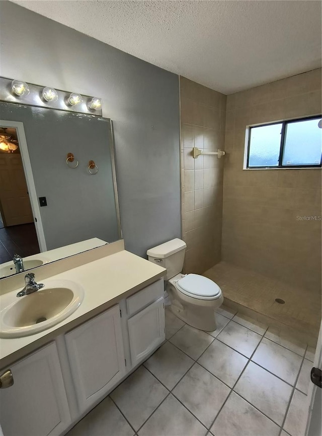 bathroom with vanity, tile patterned floors, toilet, tiled shower, and a textured ceiling