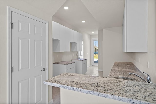 kitchen with white cabinets, sink, light stone countertops, light tile patterned floors, and kitchen peninsula