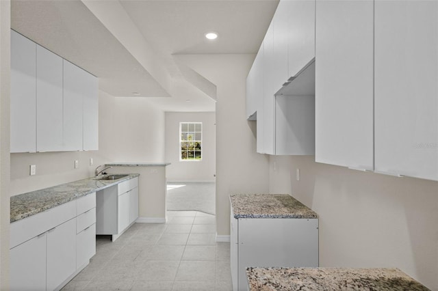 kitchen featuring white cabinets, light tile patterned flooring, light stone countertops, and sink