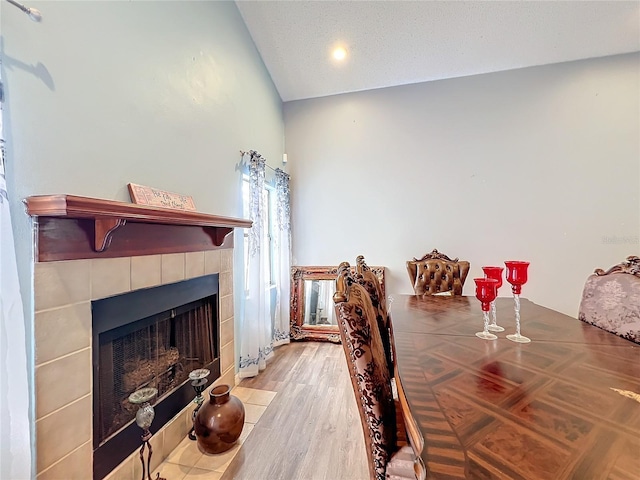 dining area featuring a textured ceiling, a fireplace, light hardwood / wood-style floors, and lofted ceiling