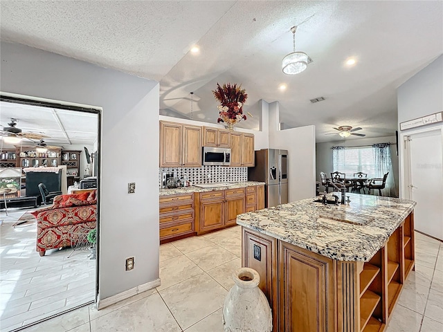 kitchen with light stone counters, a textured ceiling, stainless steel appliances, vaulted ceiling, and a center island with sink