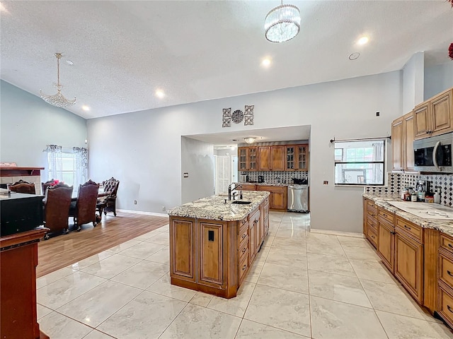 kitchen featuring light stone counters, a textured ceiling, pendant lighting, light hardwood / wood-style flooring, and an island with sink