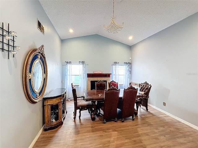 dining room featuring hardwood / wood-style floors, lofted ceiling, a textured ceiling, and a tile fireplace