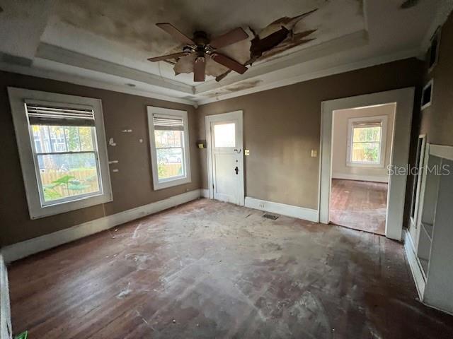 interior space with ceiling fan, a healthy amount of sunlight, ornamental molding, and a tray ceiling