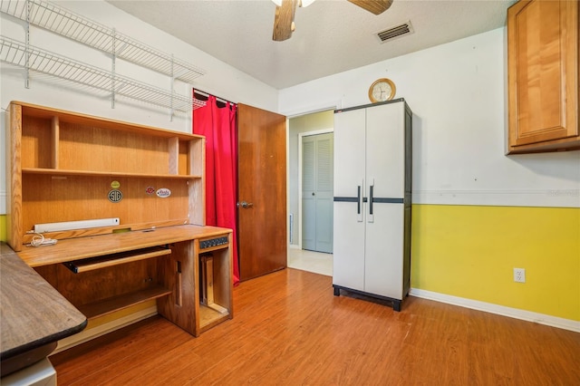 unfurnished office with a textured ceiling, built in desk, light hardwood / wood-style flooring, and ceiling fan