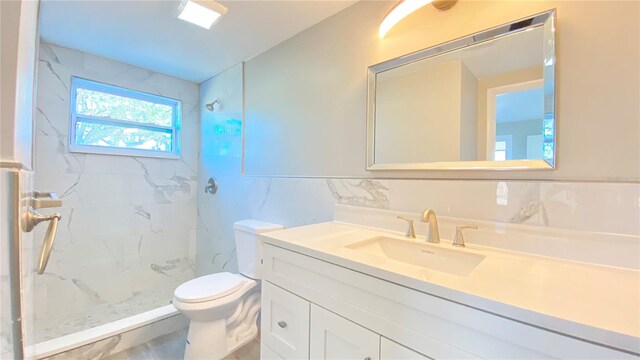 bathroom featuring a tile shower, vanity, tile walls, and toilet