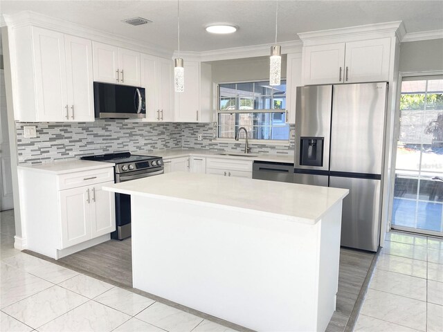 kitchen with sink, appliances with stainless steel finishes, decorative light fixtures, a kitchen island, and white cabinetry