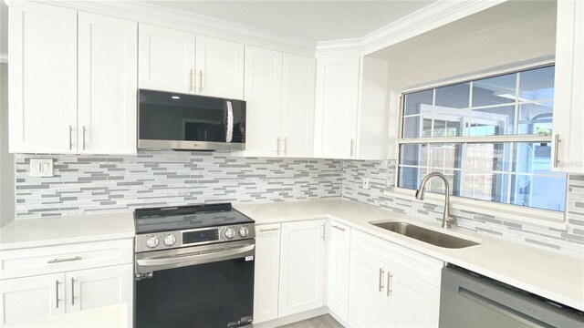 kitchen with backsplash, white cabinets, crown molding, sink, and stainless steel appliances