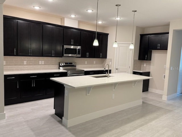 kitchen with sink, pendant lighting, decorative backsplash, a center island with sink, and appliances with stainless steel finishes